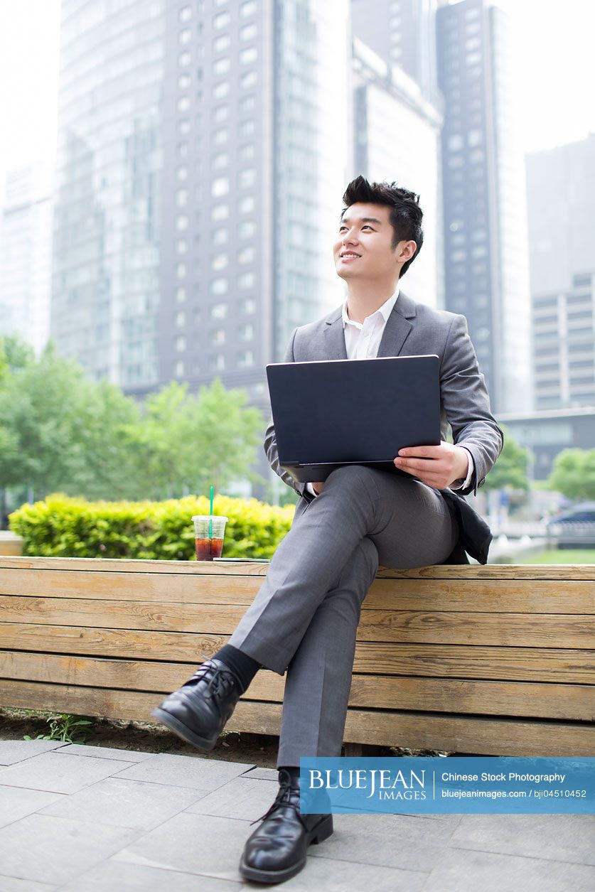 Young Chinese businessman working with laptop outdoors