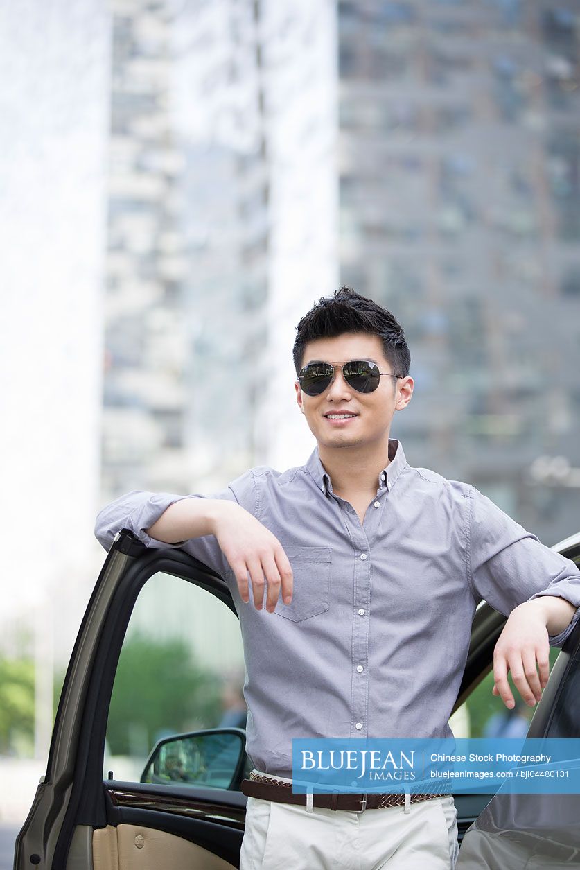 Young Chinese man standing next to his car