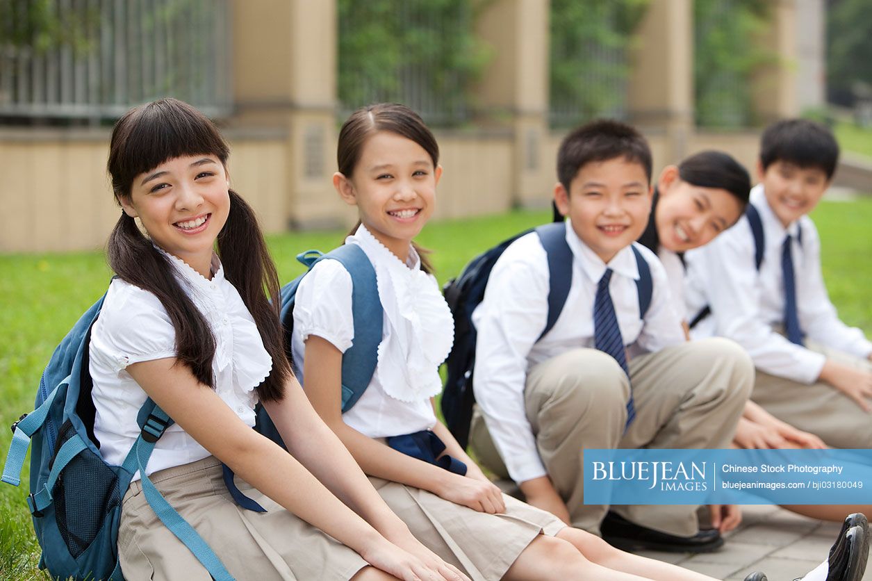 Lively Chinese schoolchildren in uniform sitting on floor at school yard