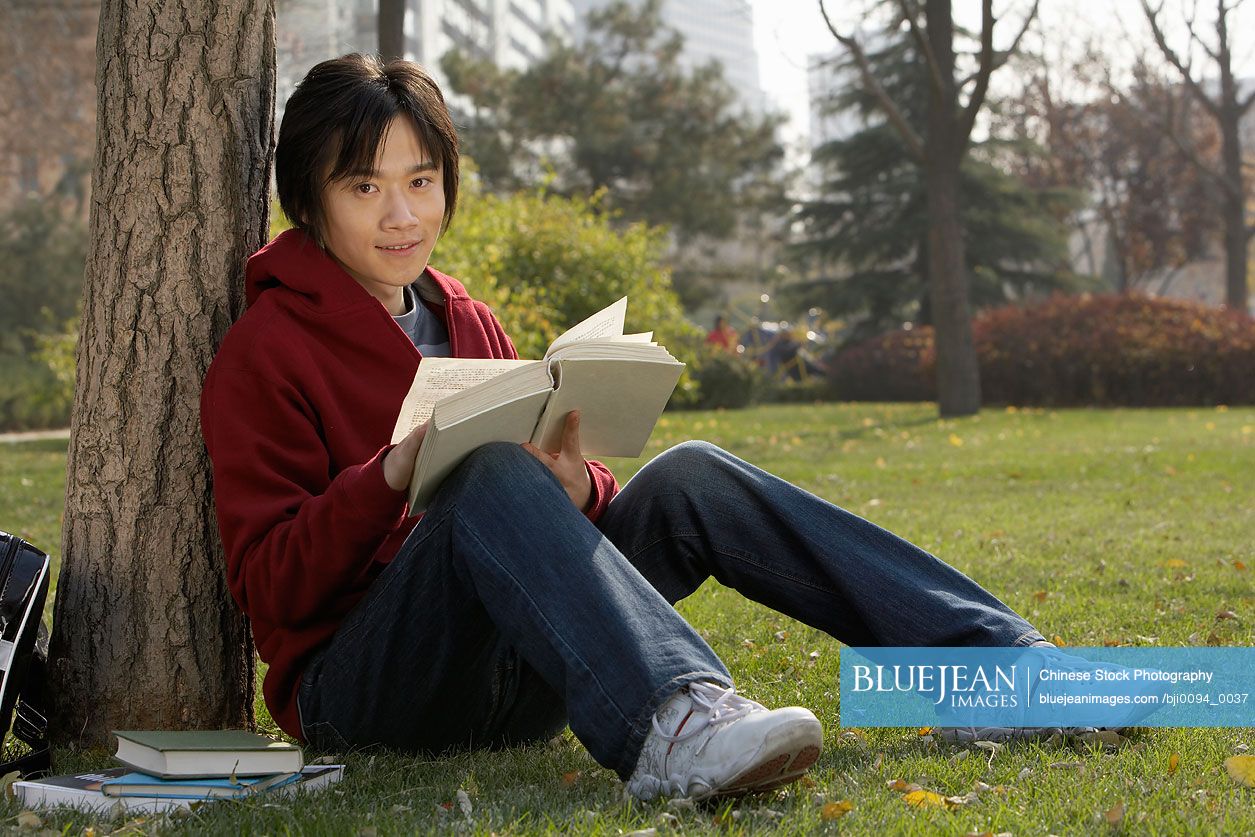 Young Chinese man reading book in the park