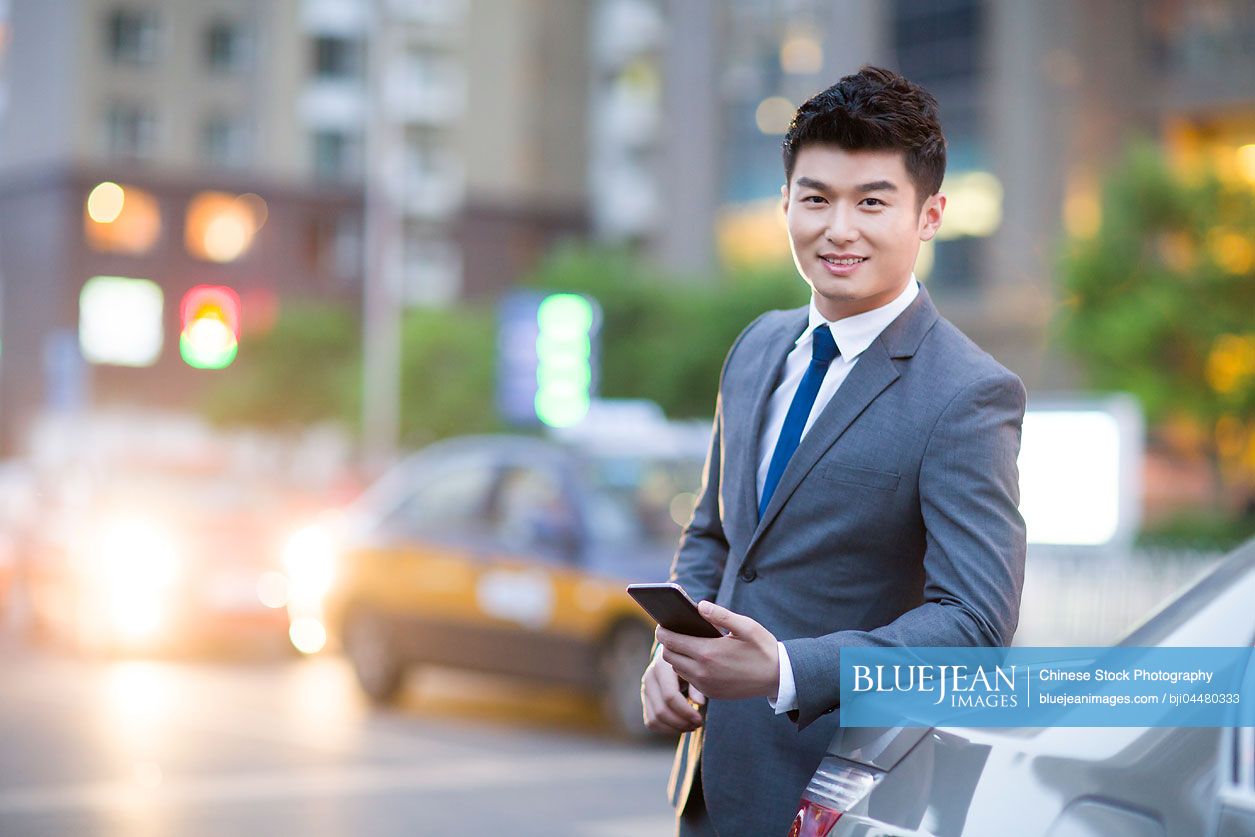Chinese businessman standing next to the car with smart phone