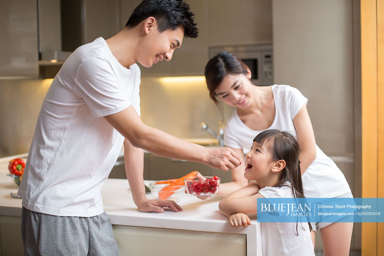 Young Chinese father feeding daughter fruit in the kitchen
