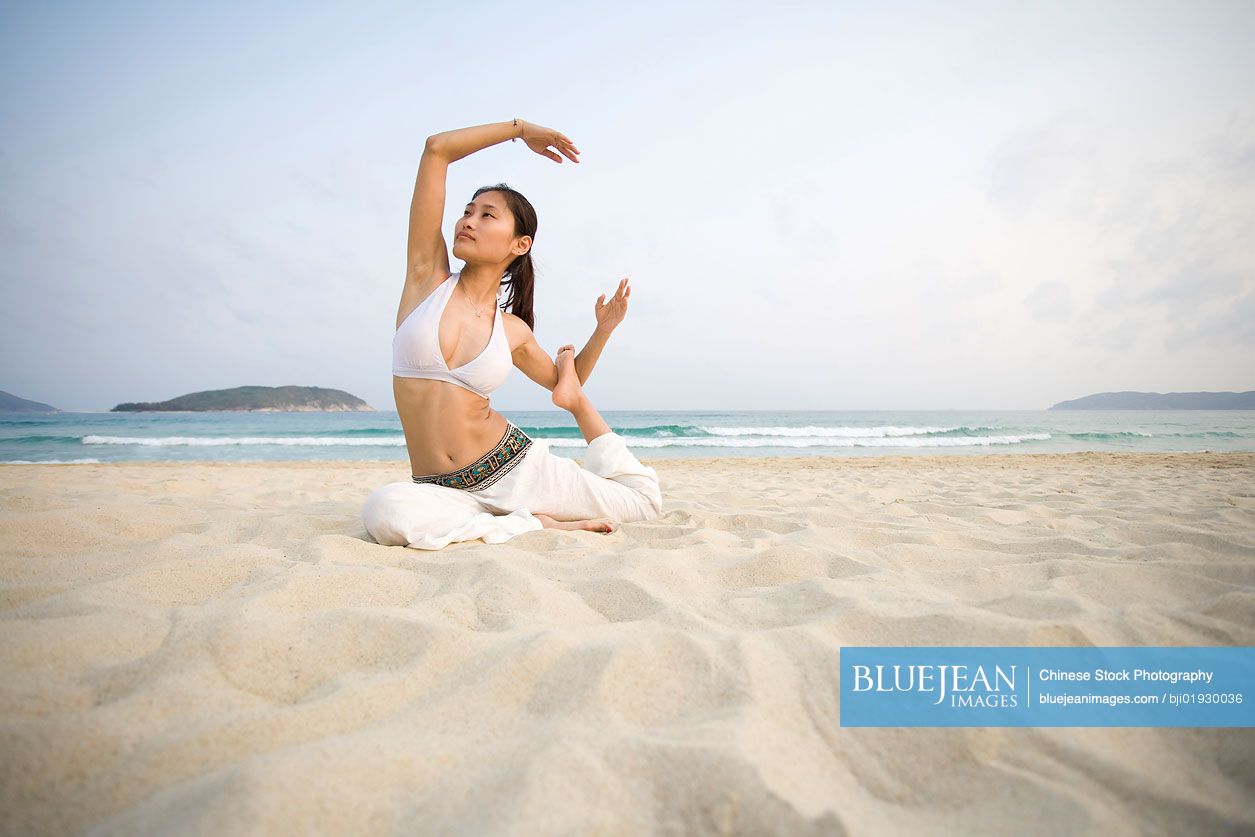 Young Chinese woman doing yoga on the beach