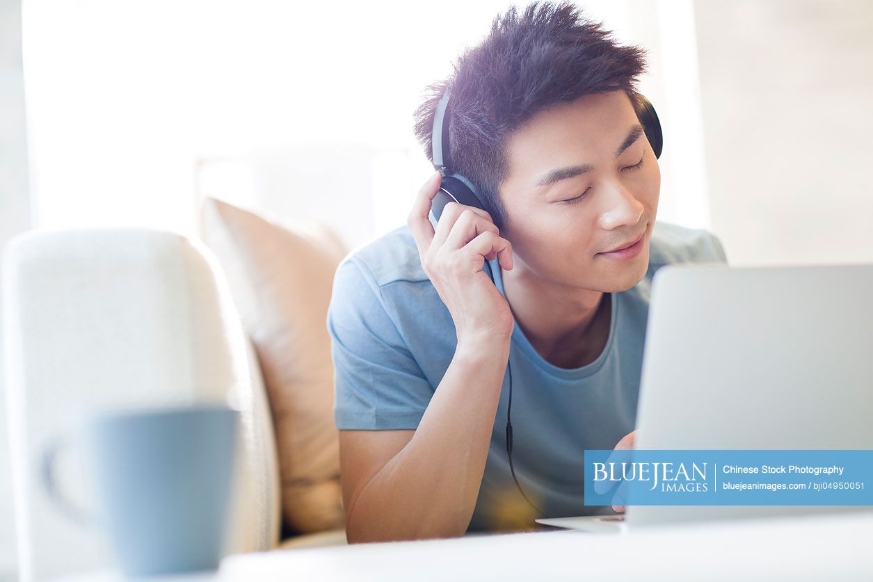 Young Chinese man listening to music with laptop on the sofa