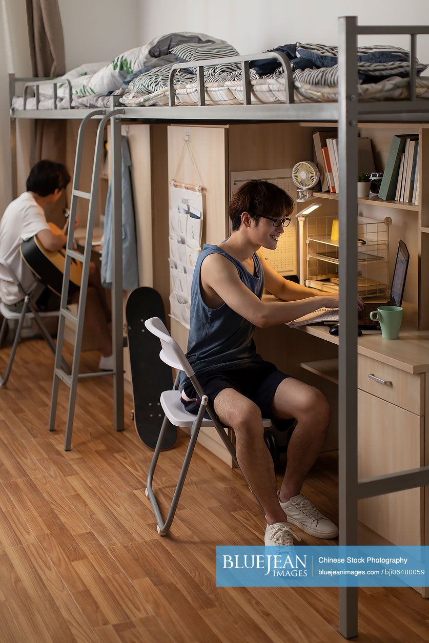 Young Chinese university student using laptop in dormitory