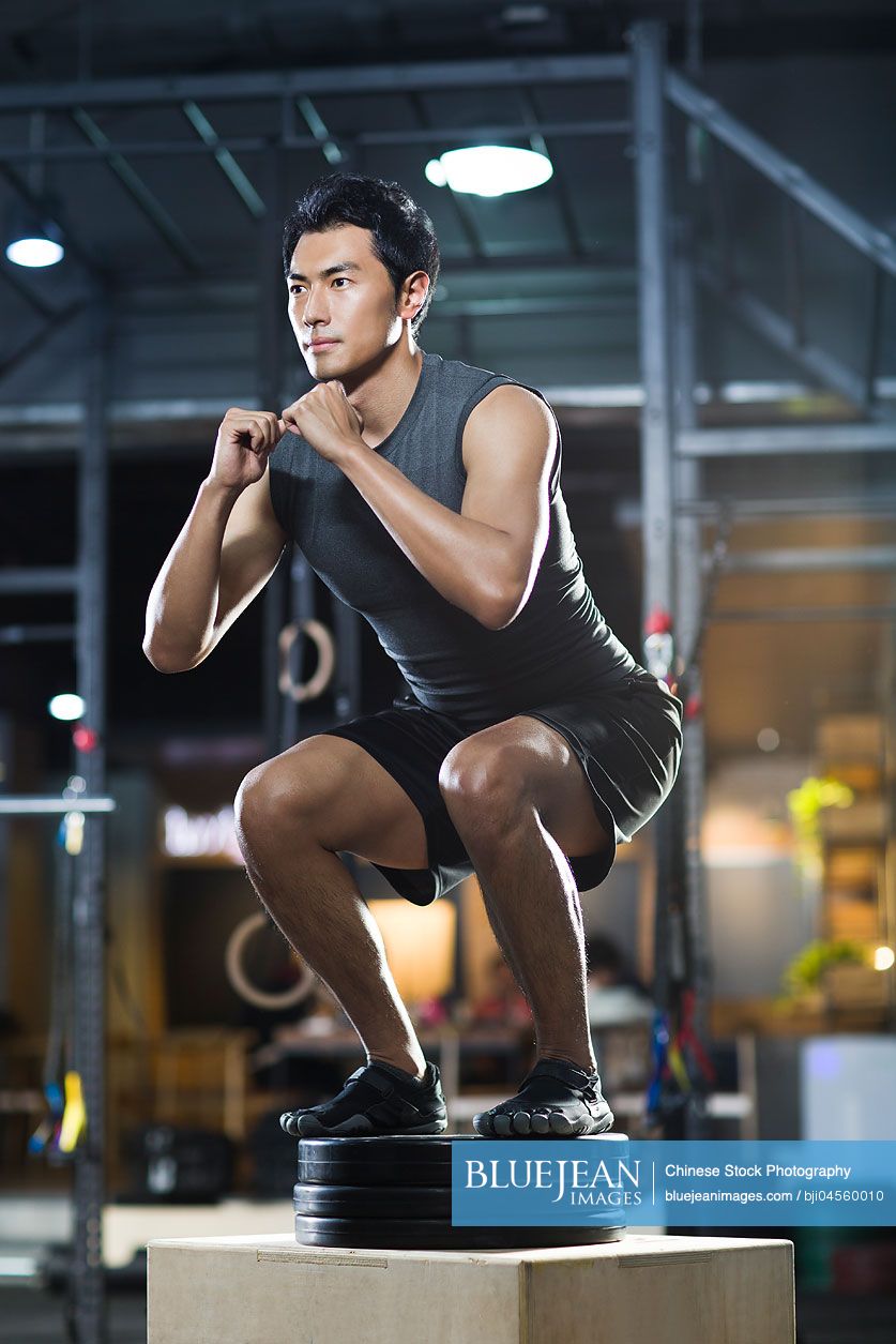 Young Chinese man doing box jump in crossfit gym