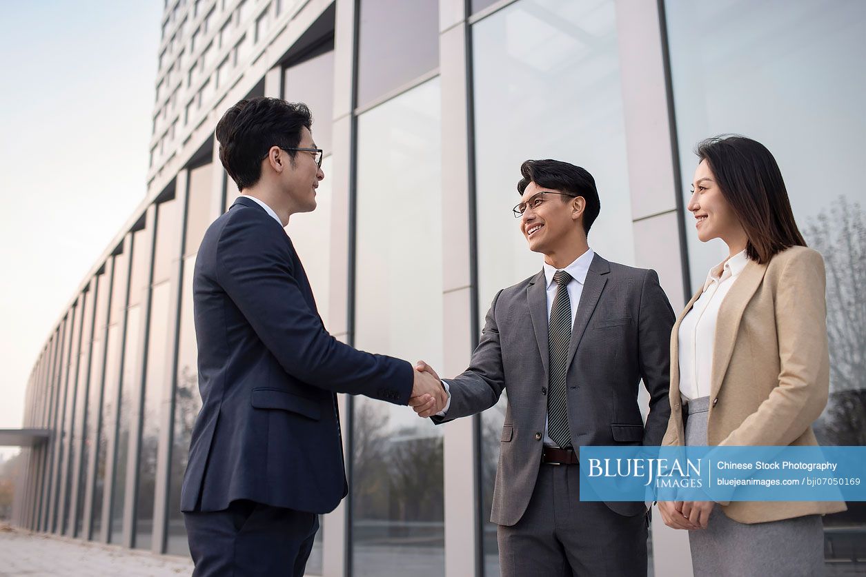 Confident Chinese business people shaking hands outdoors