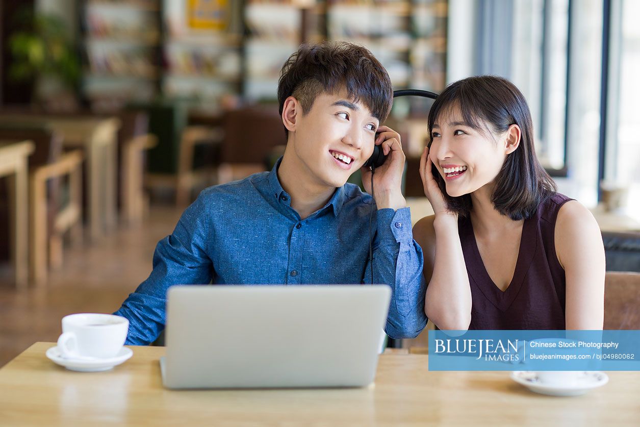 Young Chinese couple listening to music in café