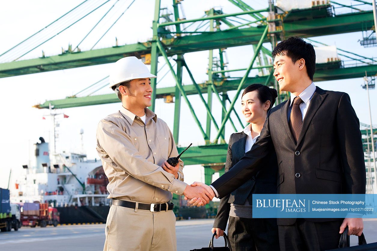 Chinese businesspeople and a shipping industry worker shaking hands at a shipping port