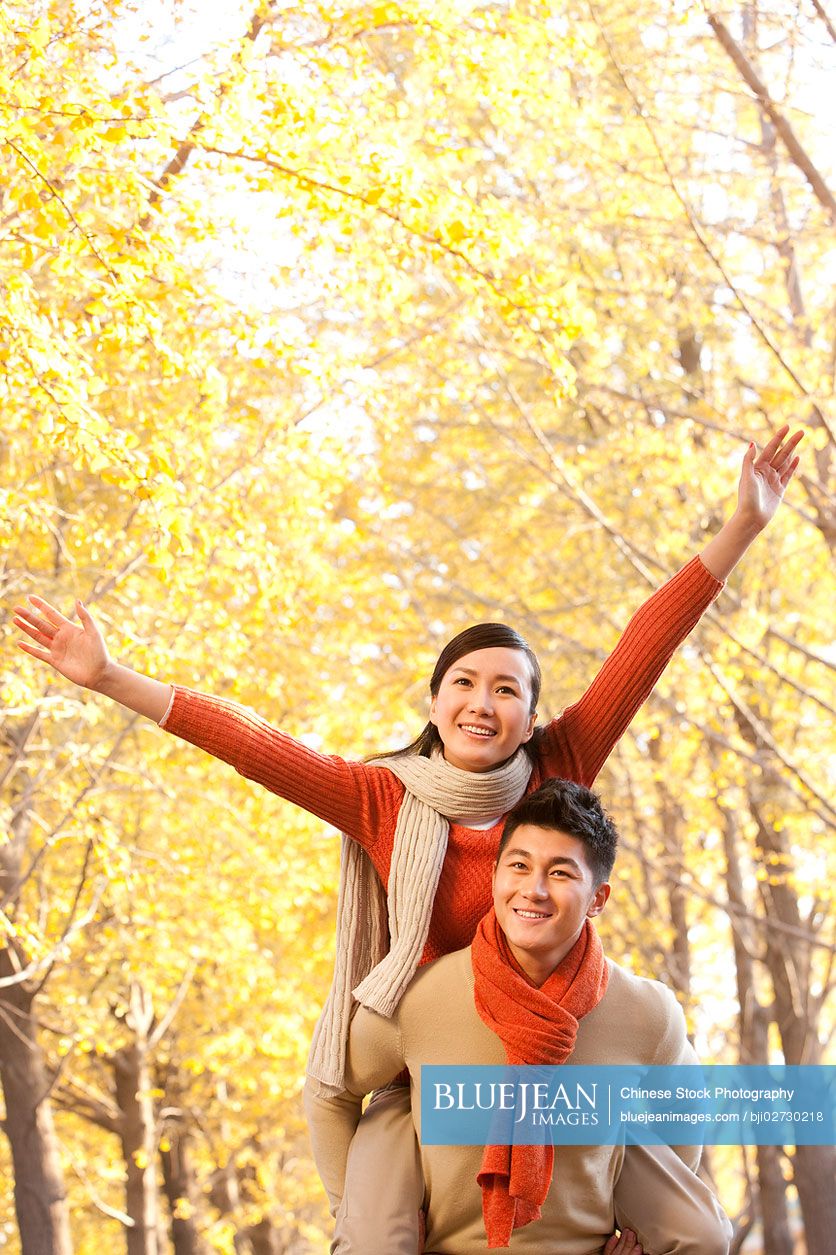 Young Chinese couple with arms outstretched, autumn leaves in the background