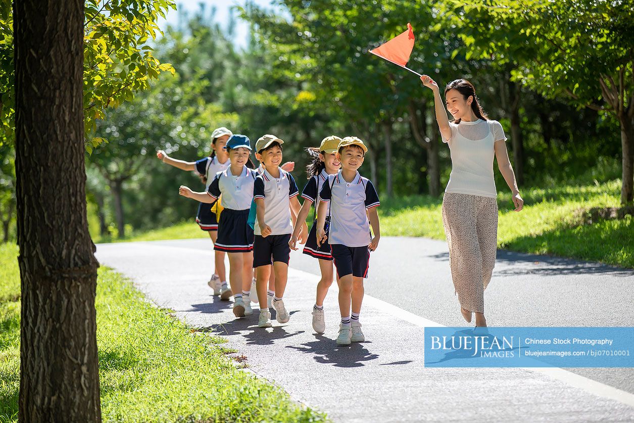 Cheerful Chinese school children walking in park with their teacher