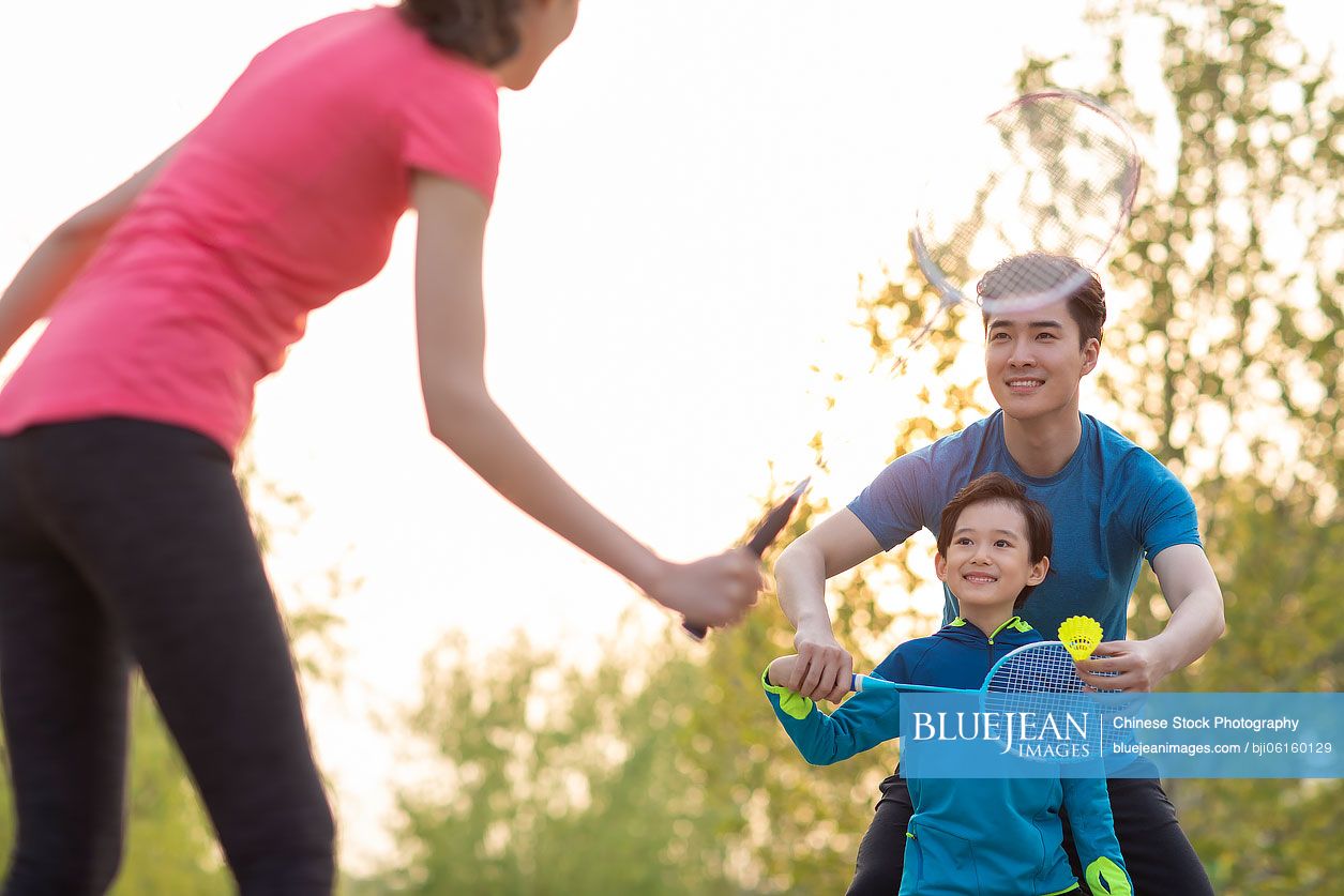 Happy young Chinese family playing badminton in park
