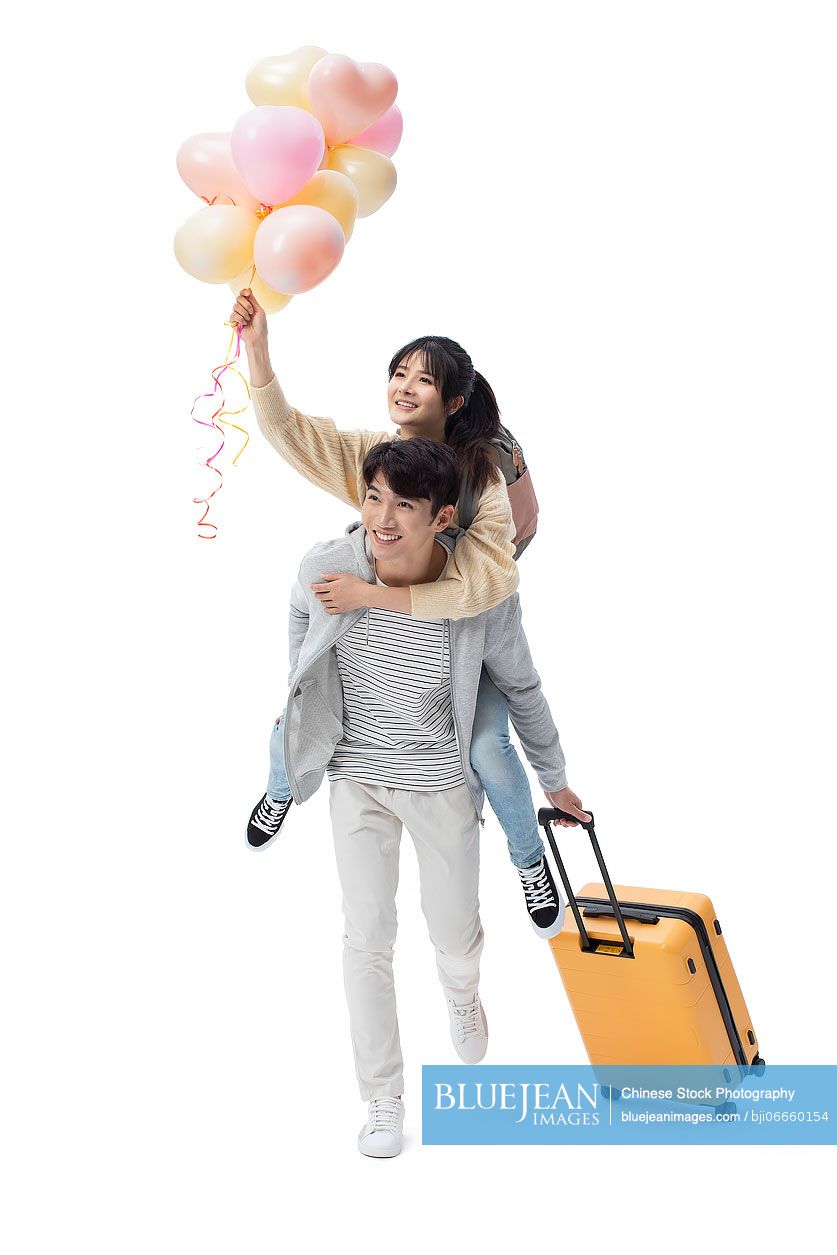 Happy young Chinese couple with wheeled luggage