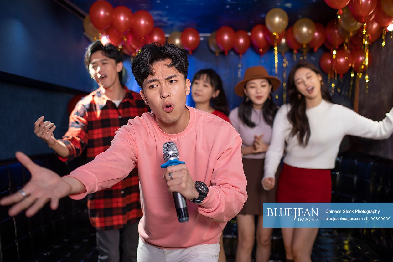 Happy young Chinese friends singing karaoke in nightclub