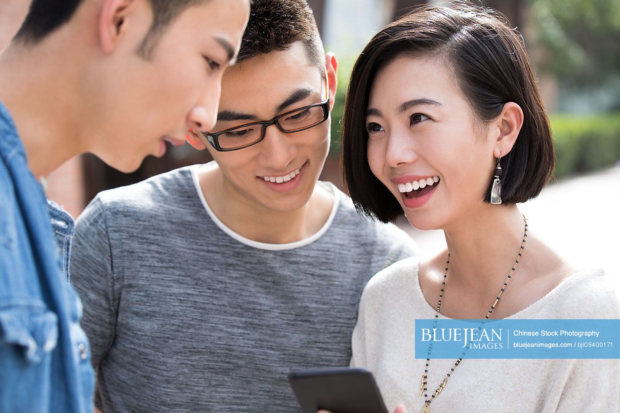 Cheerful young Chinese friends using smart phone