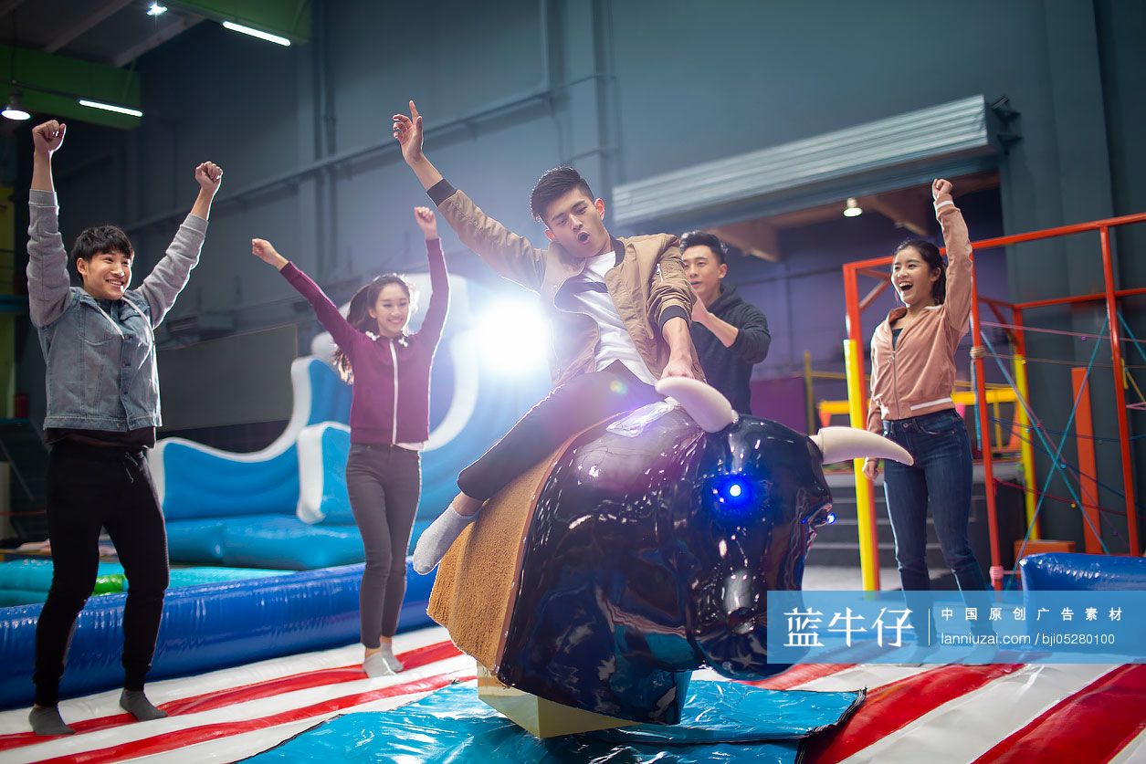 快乐的年轻朋友在游乐场玩电动骑牛机