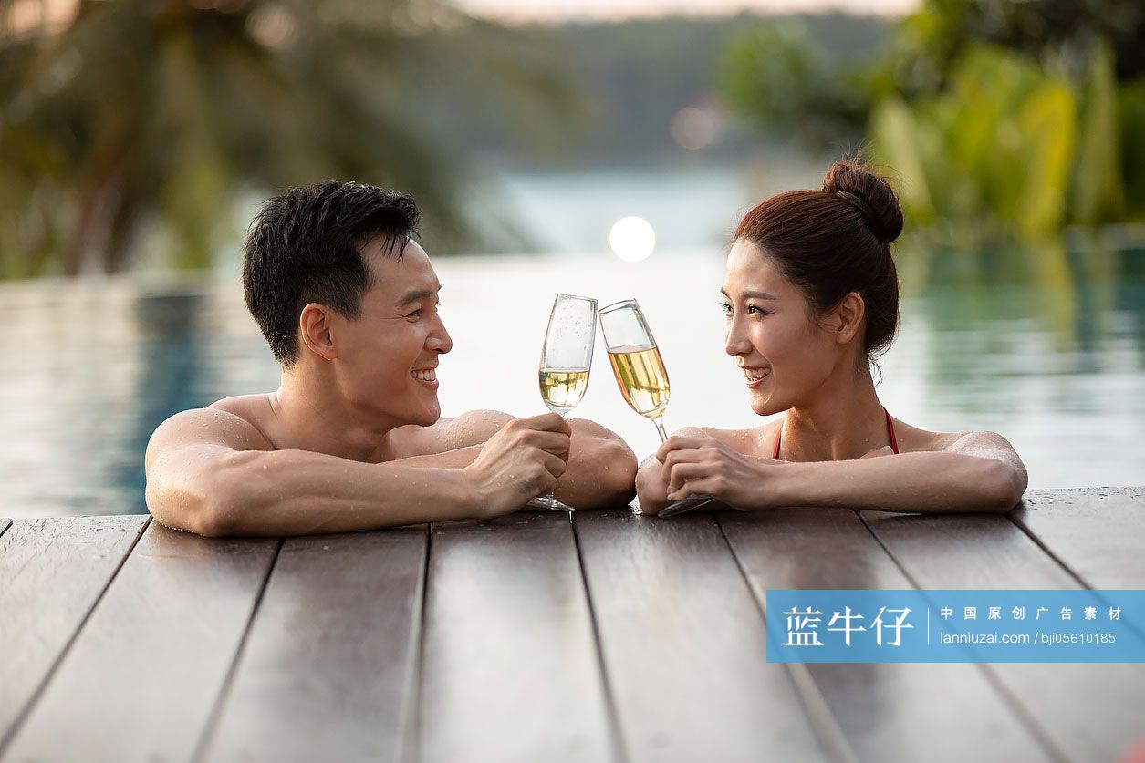 快乐的年轻情侣在泳池边喝香槟