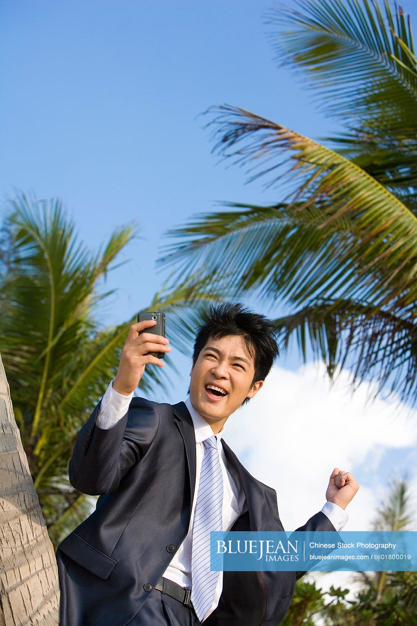 Chinese businessman with his mobile phone on the beach