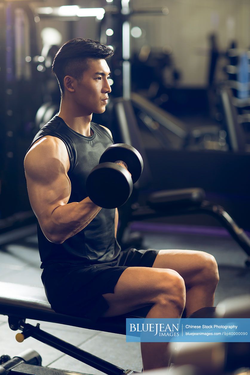 Young Chinese man working out with dumbbell at gym