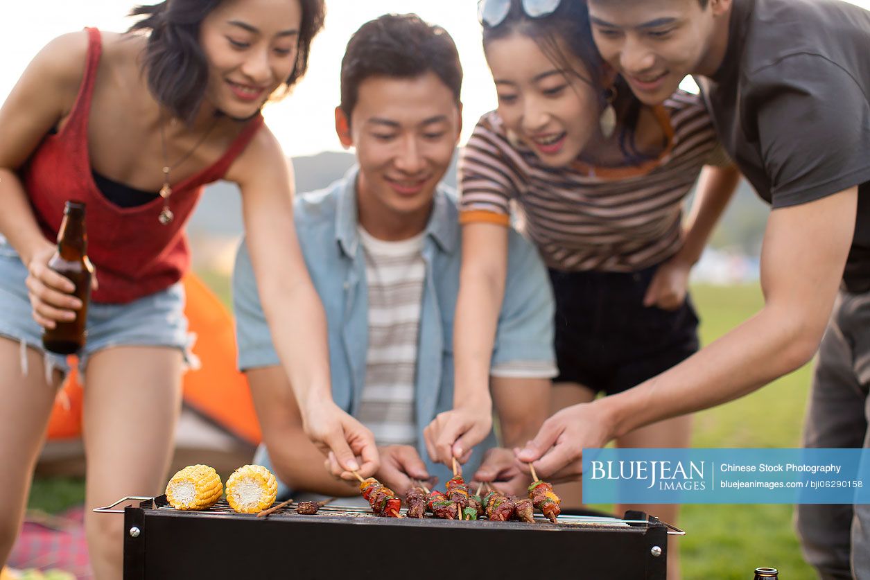 Happy young Chinese friends barbecuing outdoors