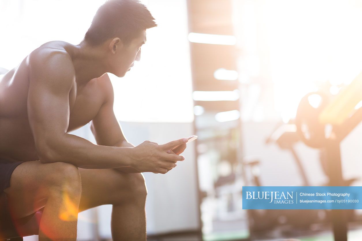 Young Chinese man using smart phone in gym