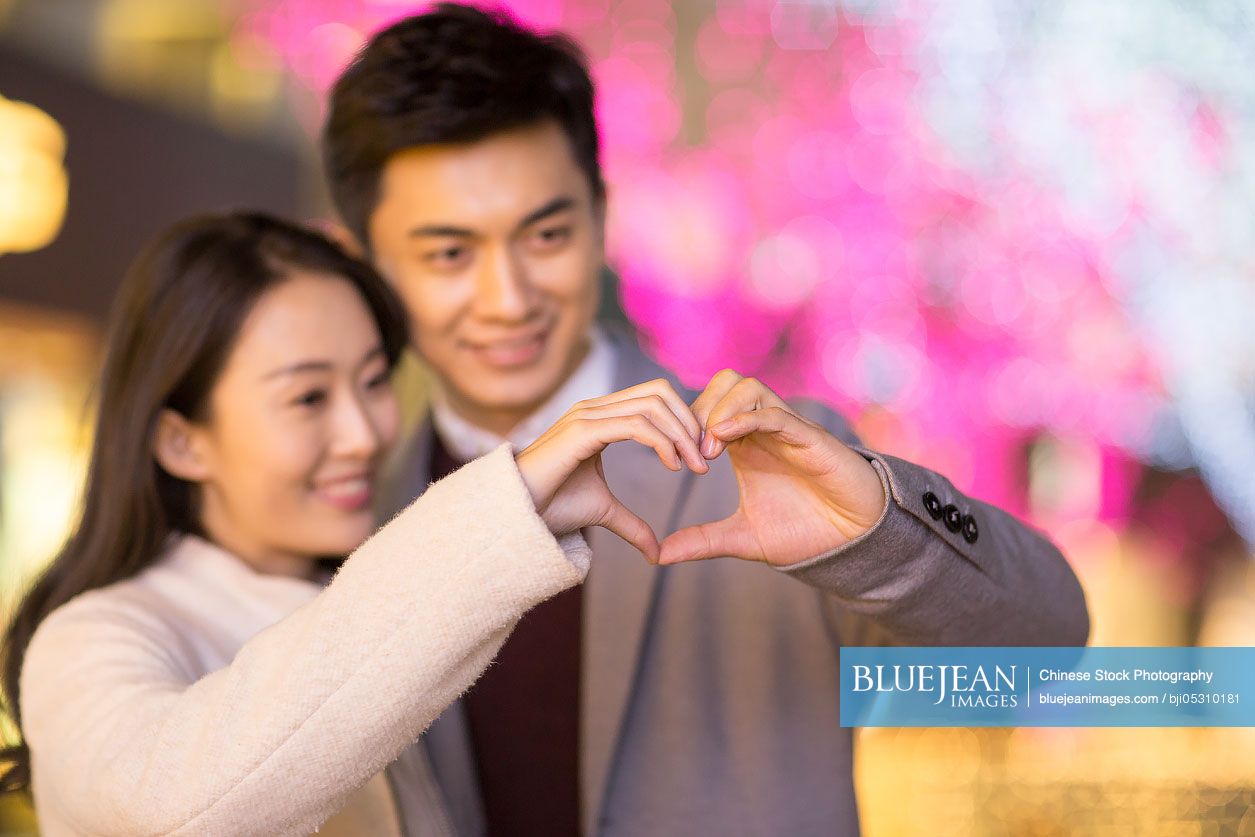 Cheerful young Chinese couple making heart shape with their hands