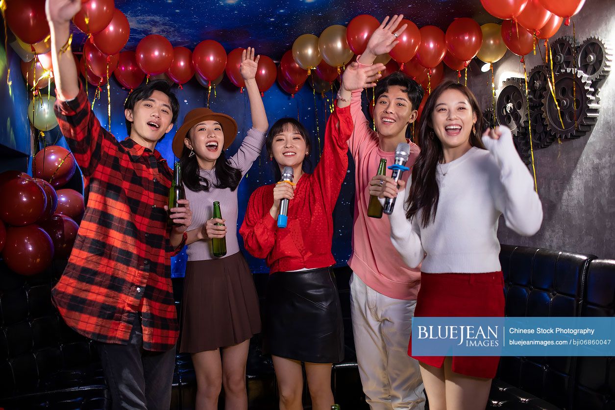 Happy young Chinese friends singing karaoke in nightclub