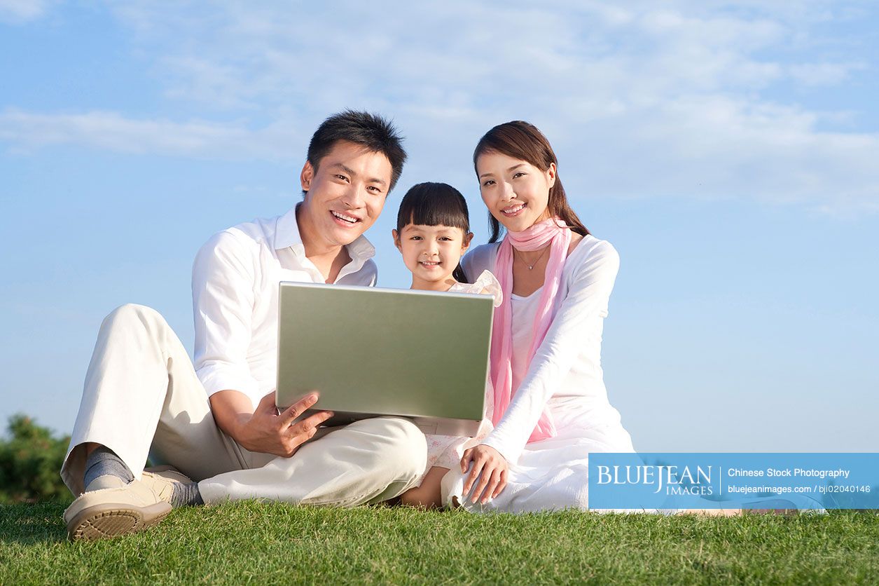 Young Chinese family using laptop in the park