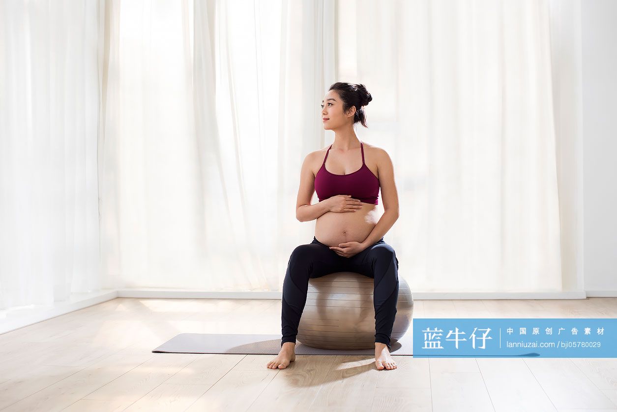 年轻孕妇坐在瑜伽球上