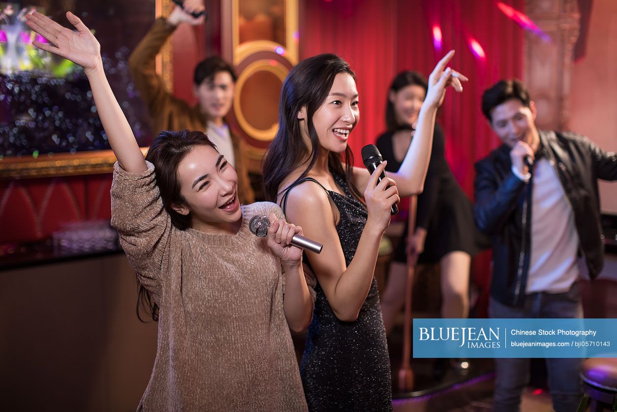 Happy Chinese friends singing karaoke in nightclub