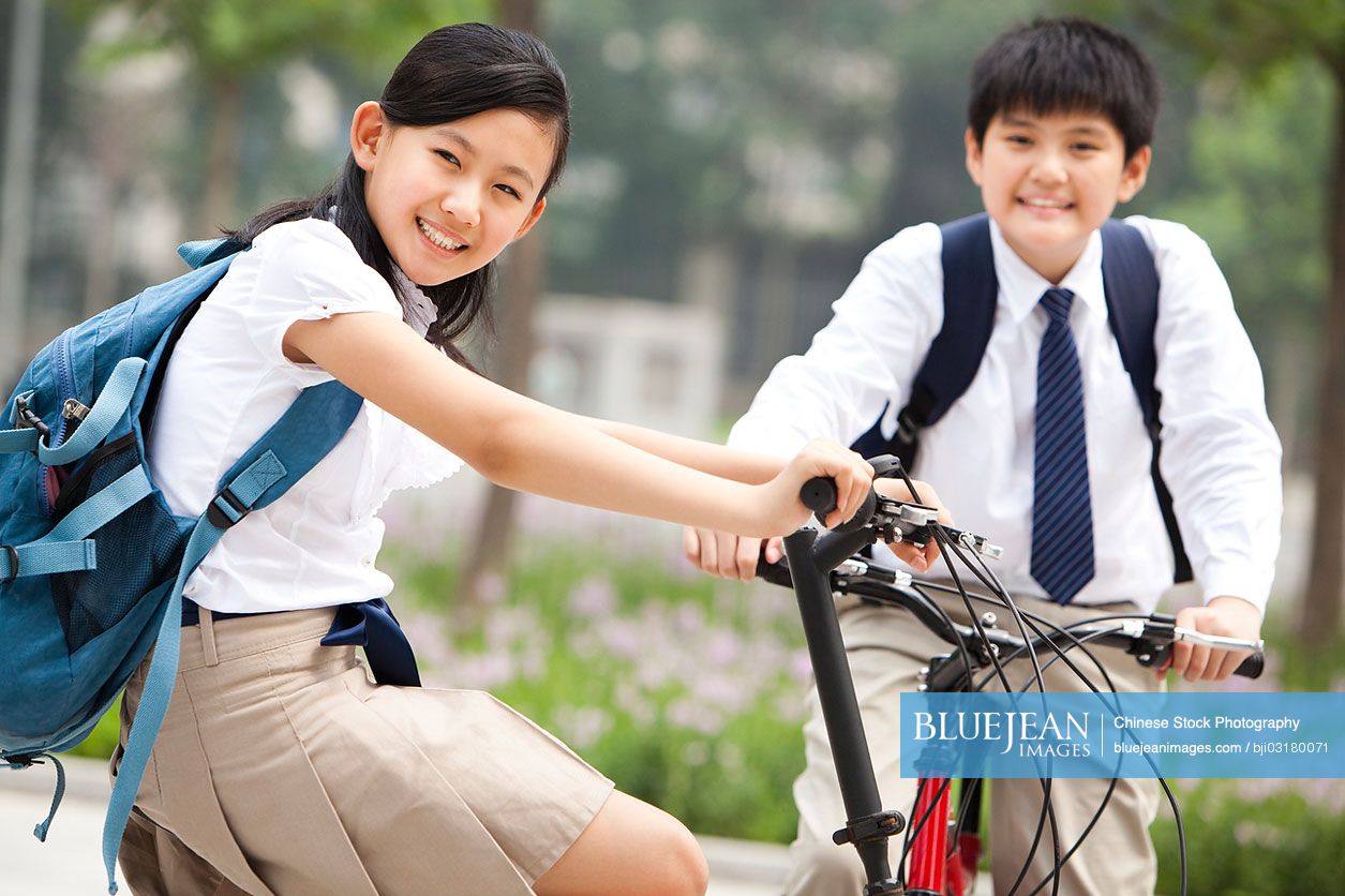 Happy Chinese schoolchildren in uniform with bicycles outdoors