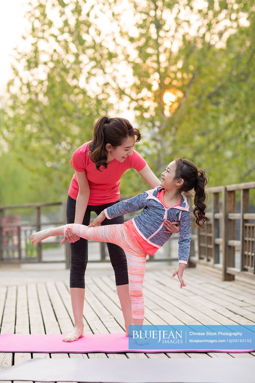 Happy Chinese mother and daughter doing yoga outdoors