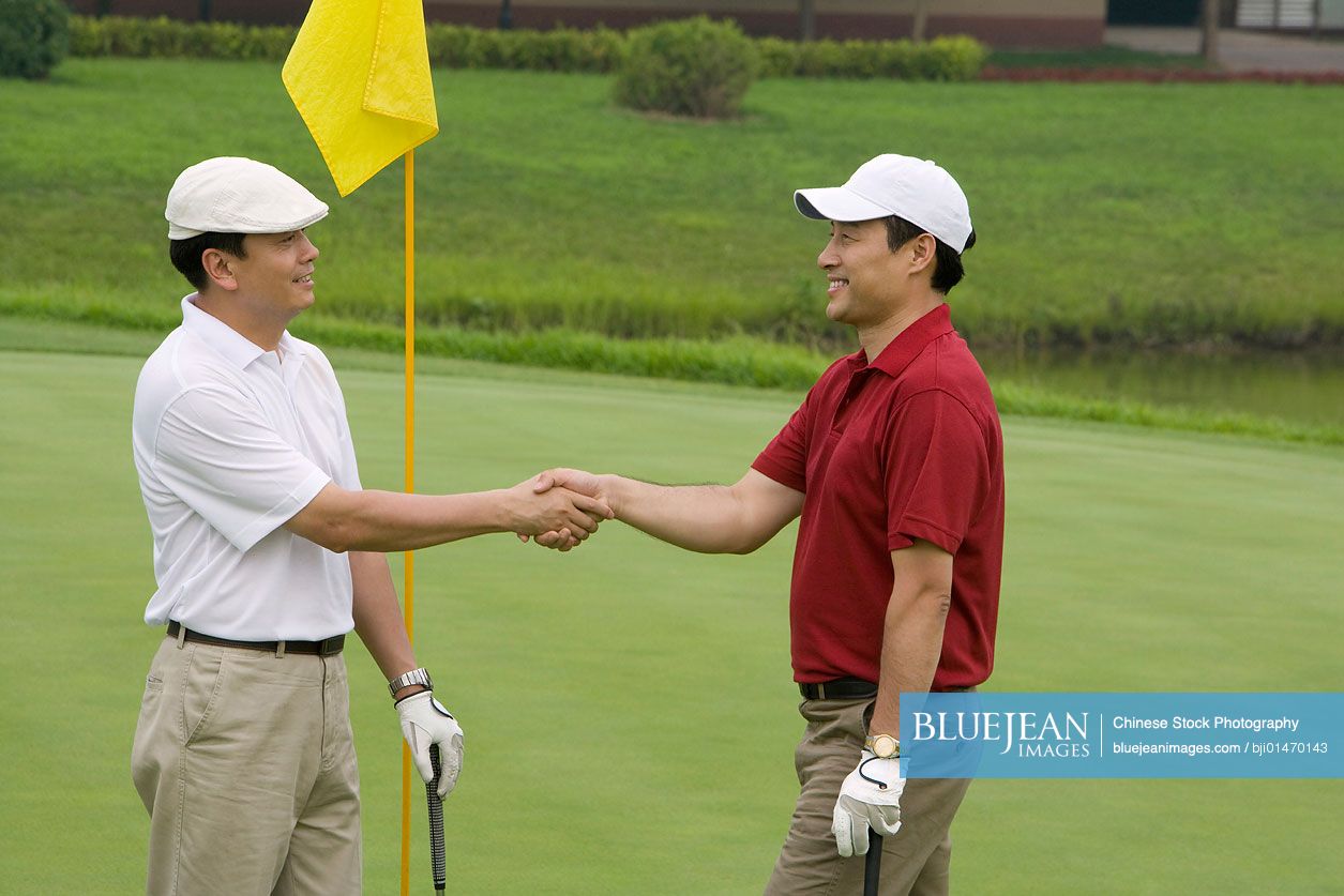 Two Chinese golfers shaking hands on the green