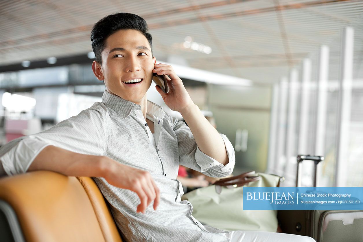 Young Chinese man talking on the phone in airport lounge