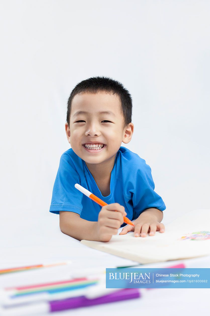 Happy little Chinese boy coloring while lying on the floor