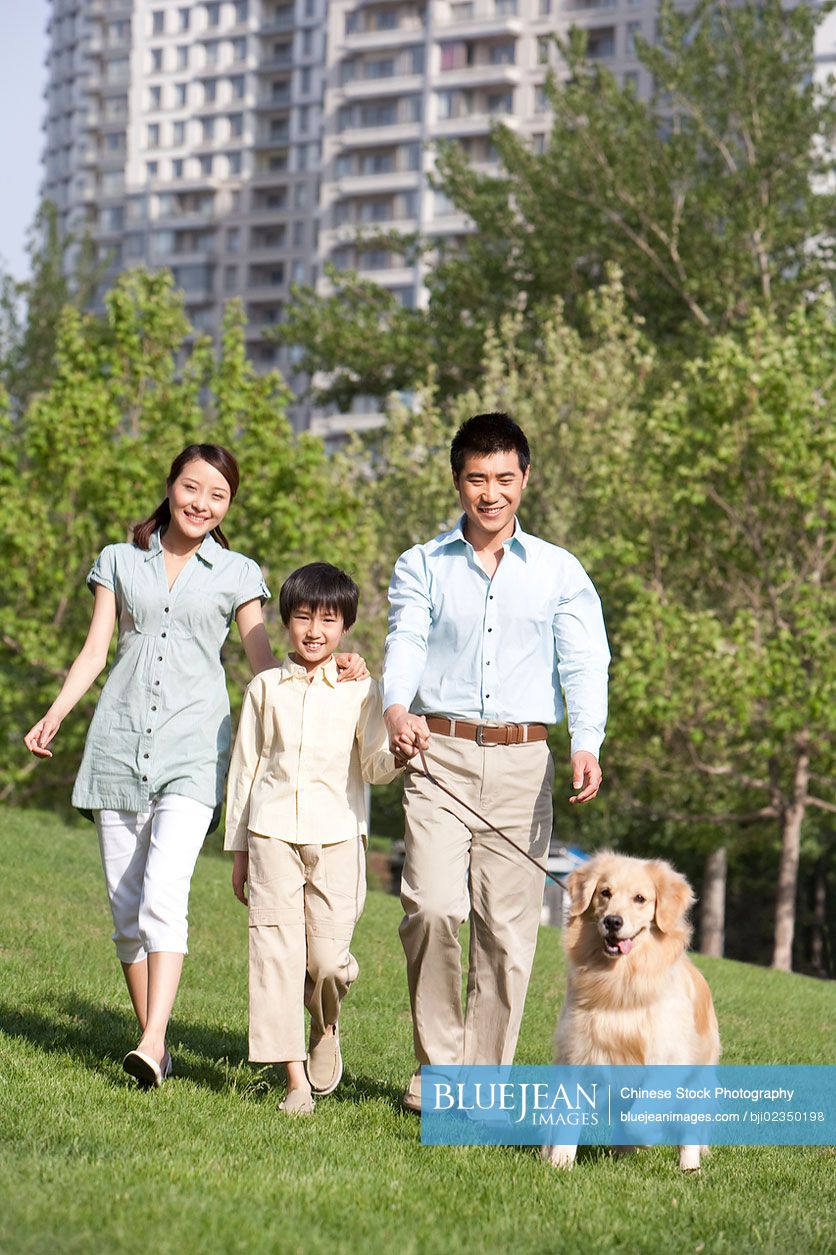 Happy Chinese family walking dog in the park