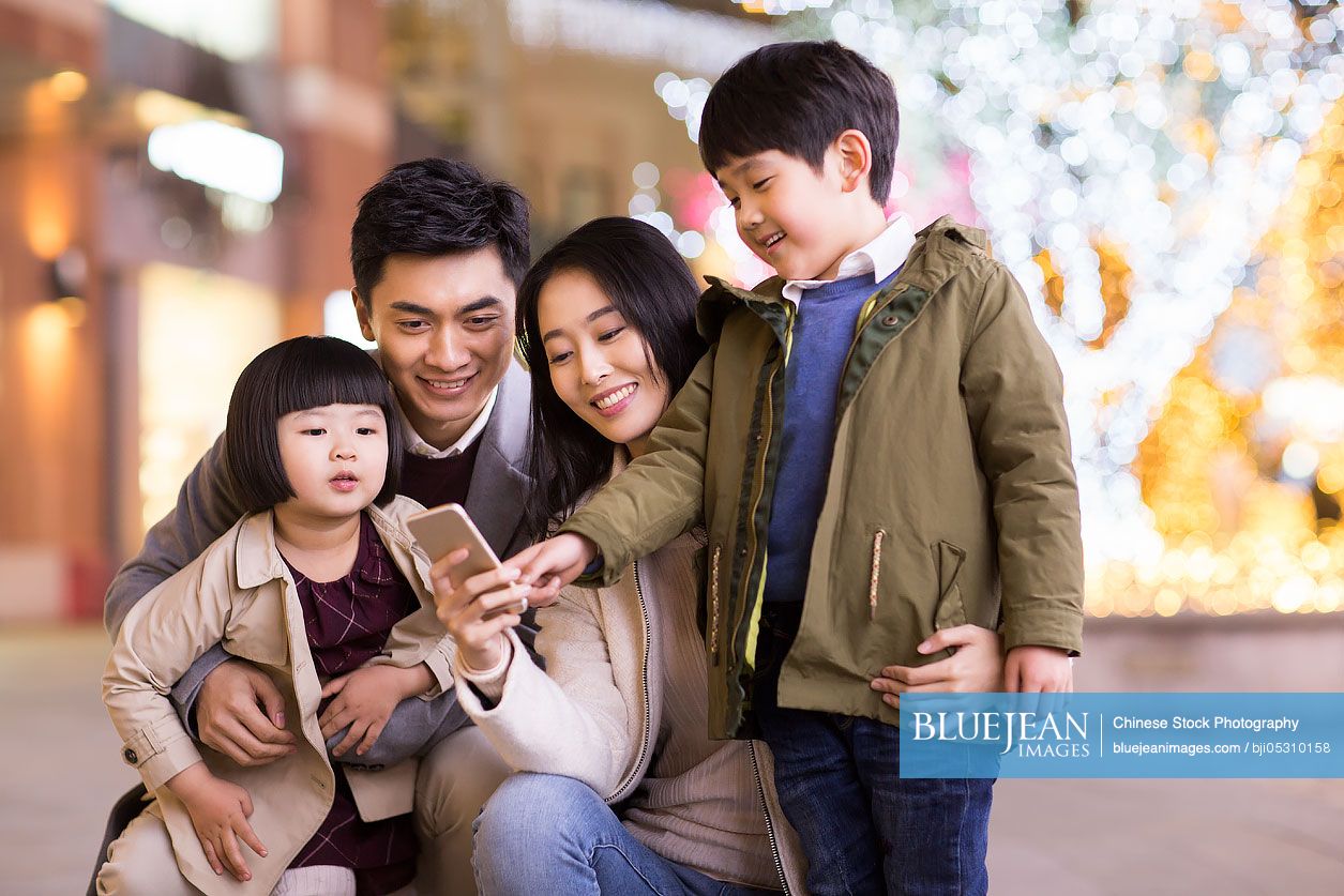 Cheerful young Chinese family using smart phone