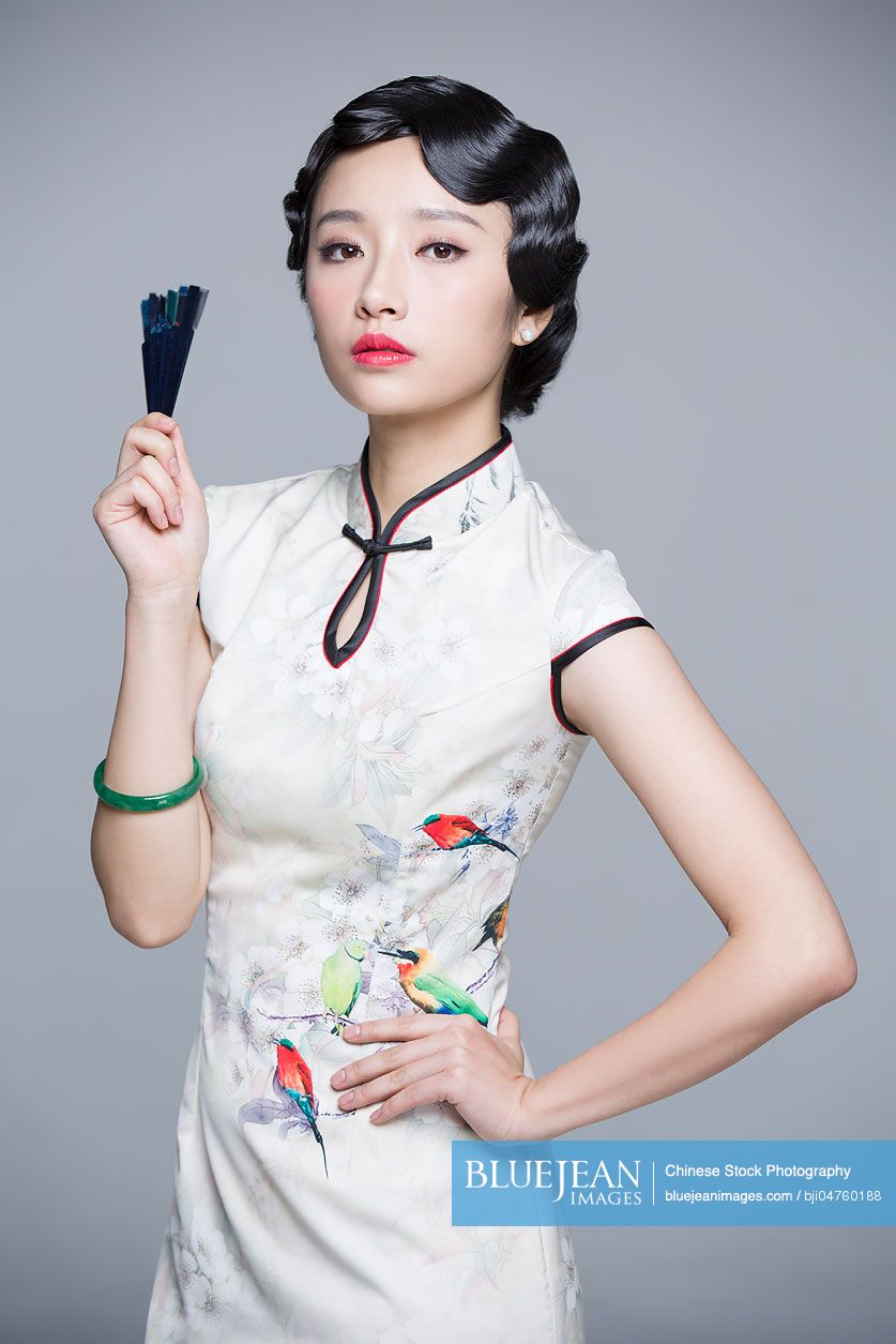 Young beautiful Chinese woman in traditional cheongsam with folding fan