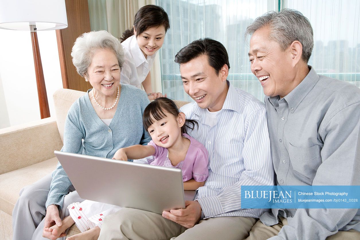 Chinese grandparents and parents with daughter looking at Laptop on a sofa