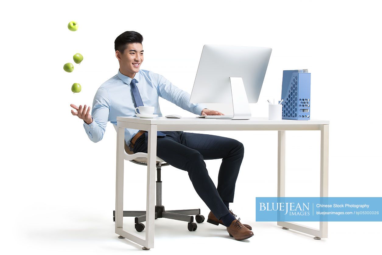 Young Chinese businessman working with computer in office juggling apples