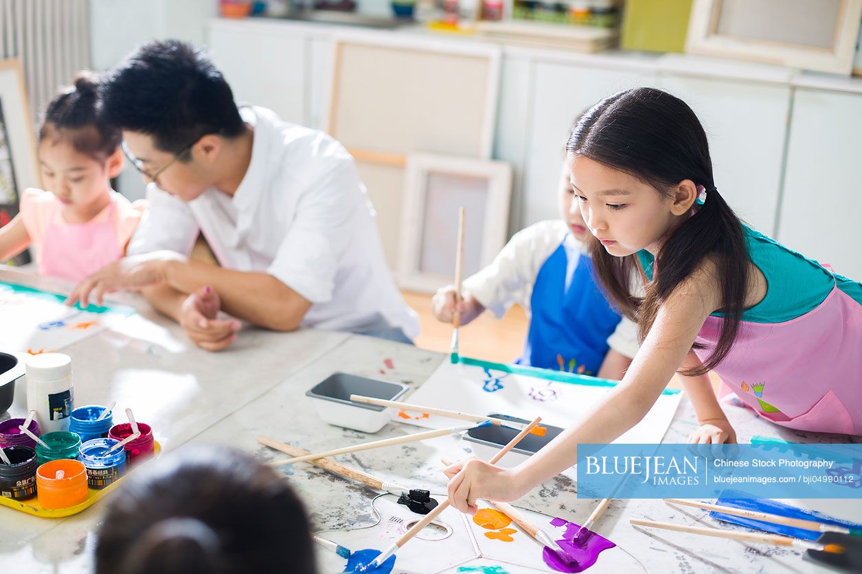 Little Chinese children painting in art class with teacher