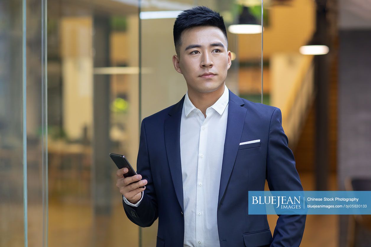 Confident young Chinese businessman using smart phone