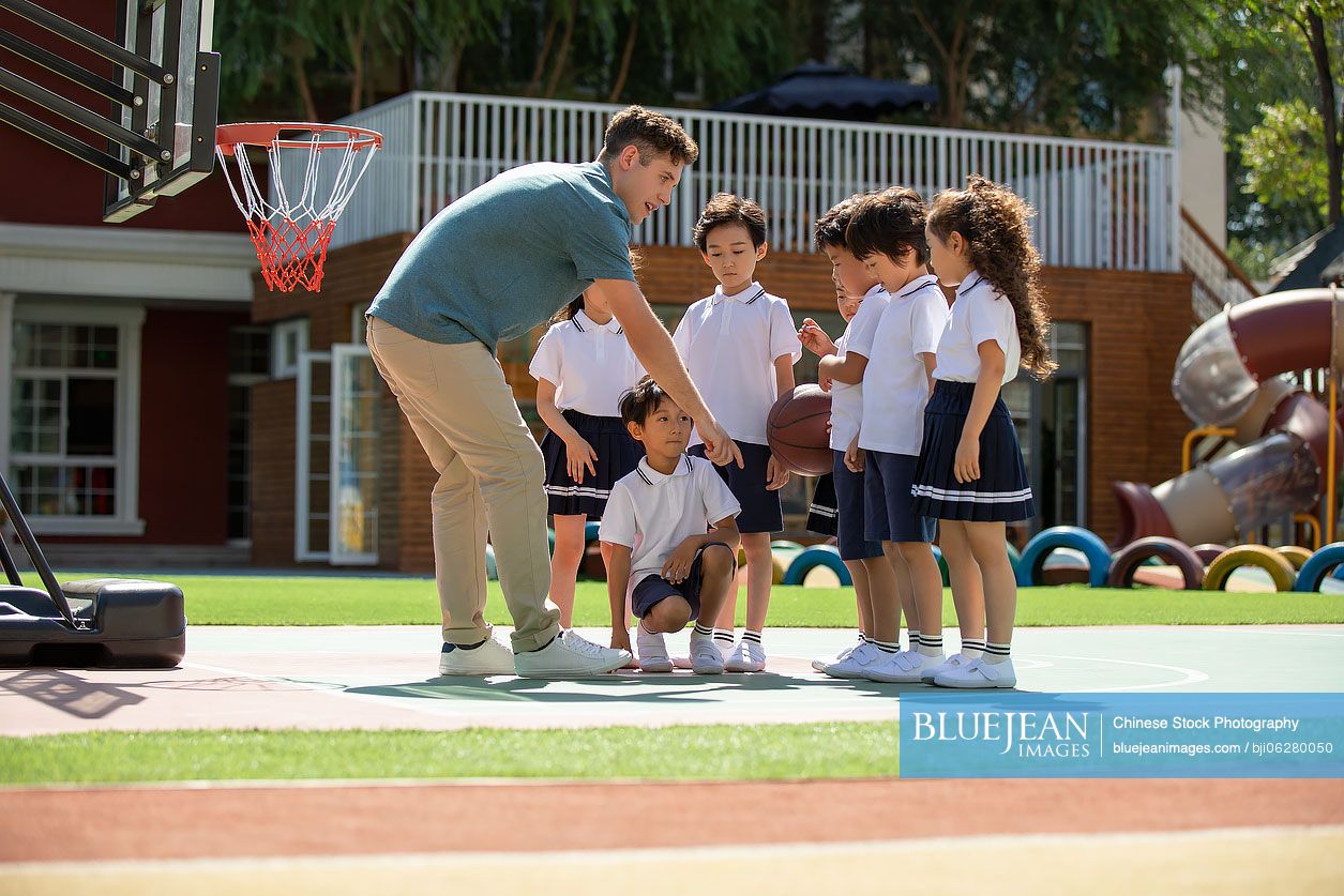 Foreign teacher teaching children basketball in playground