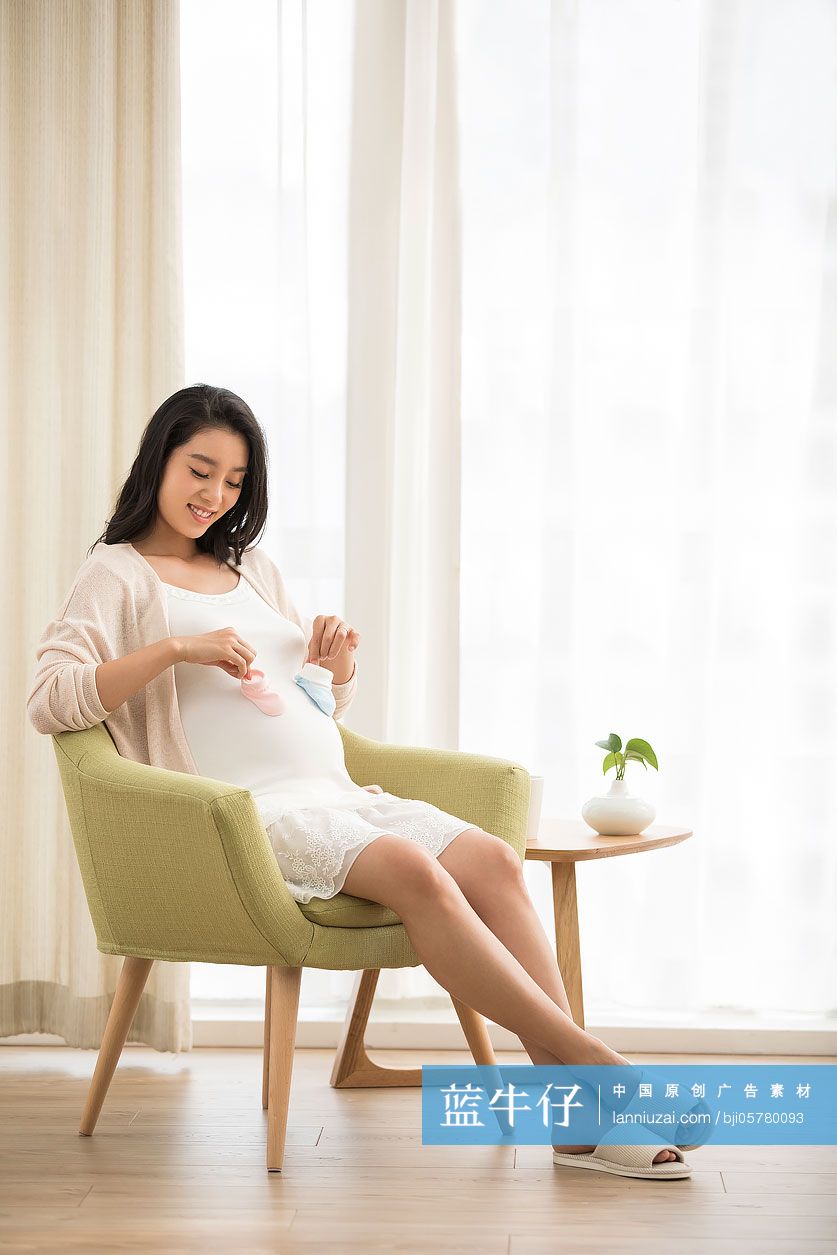 年轻孕妇拿着蓝色和粉色的婴儿袜