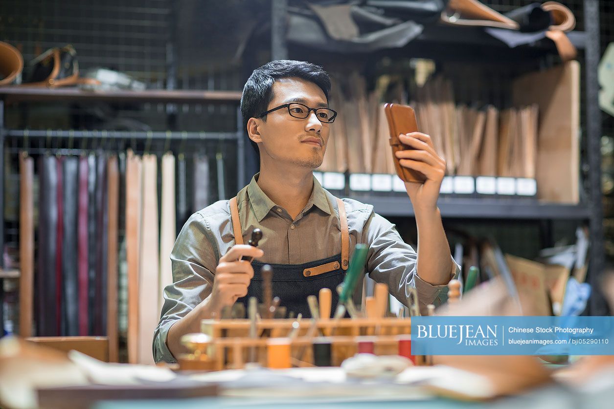 Young Chinese leather craftsman working in studio 