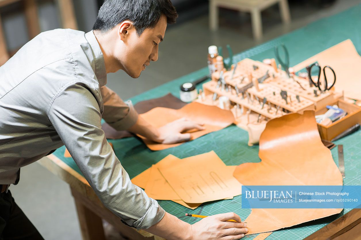 Confident Chinese leather craftsman drawing sketch in studio 
