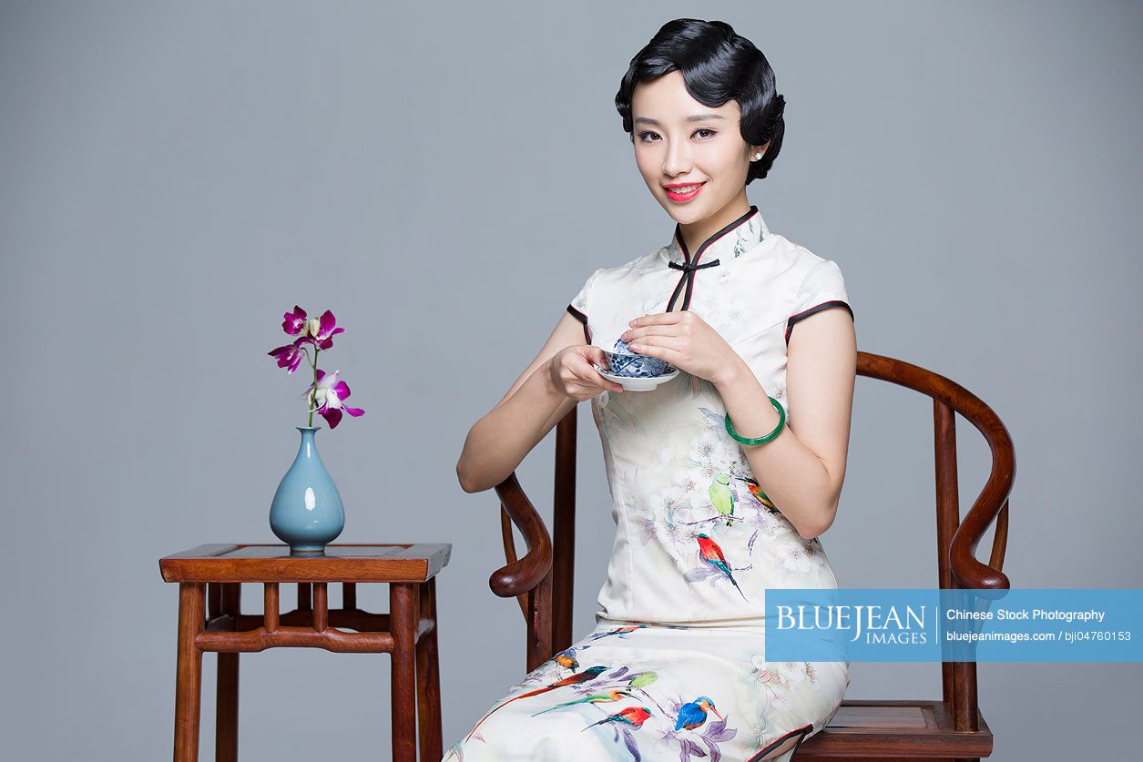 Young beautiful Chinese woman in traditional cheongsam drinking tea