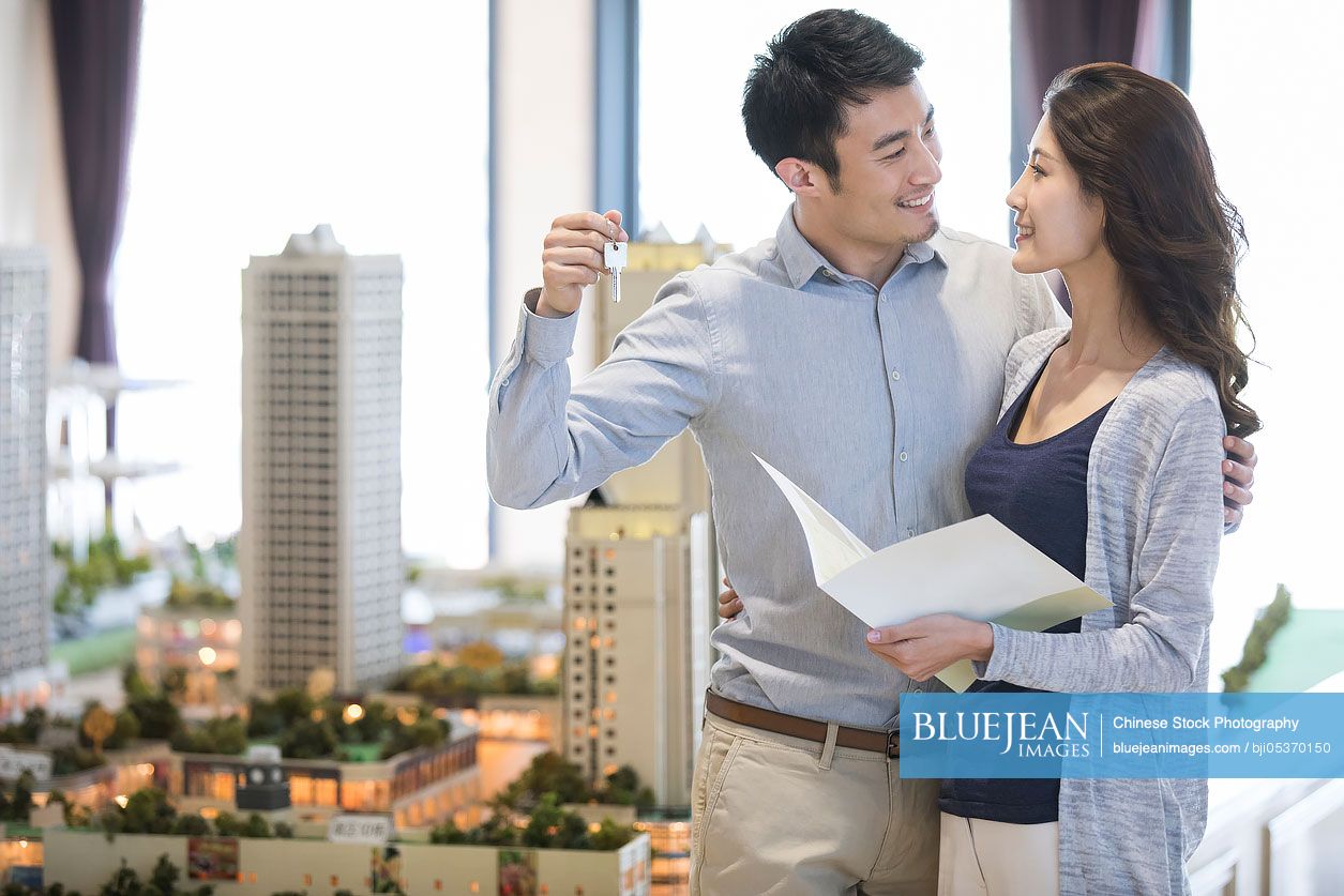 Happy young Chinese couple buying new house from sales center