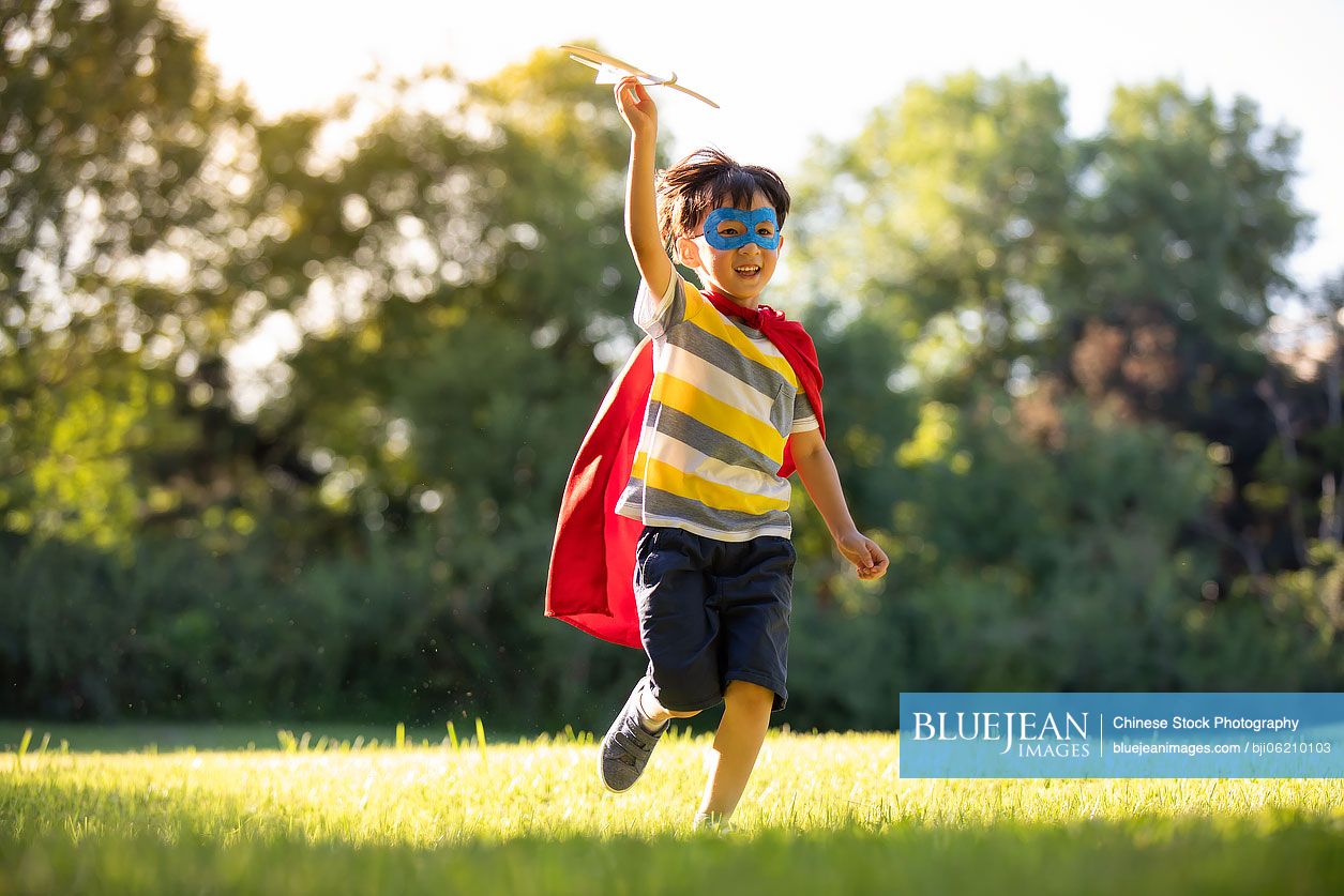 Little Chinese boy in superman costume playing on meadow