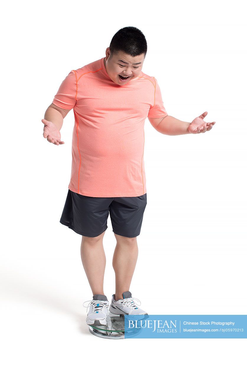 Overweight young Chinese man weighing himself on a scale-High-res